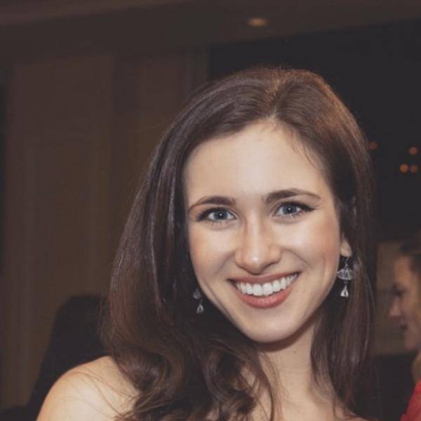 A photograph of Cathryn Haight smiling at the camera. She is wearing a strapless dark red velvet dress and dangle earrings.