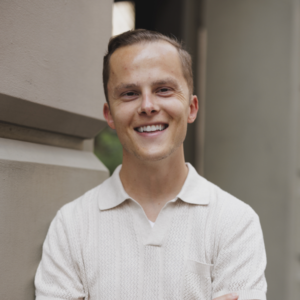 Robbie is looking at the camera smiling, he is wearing a white t- shirt. He has short blond hair.