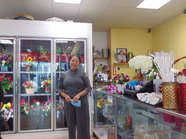 A photo of Kim's Flower Shop with Vivian standing in the shop and smiling to the camera.